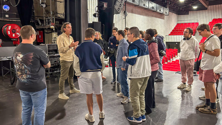 photo d'un groupe de personnes sur une scène de spectacle, l'un d'entre eux est en train de parler au reste du groupe